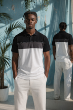 Man wearing a celvin klein black and white striped polo shirt and white pants standing in front of a blue curtain.